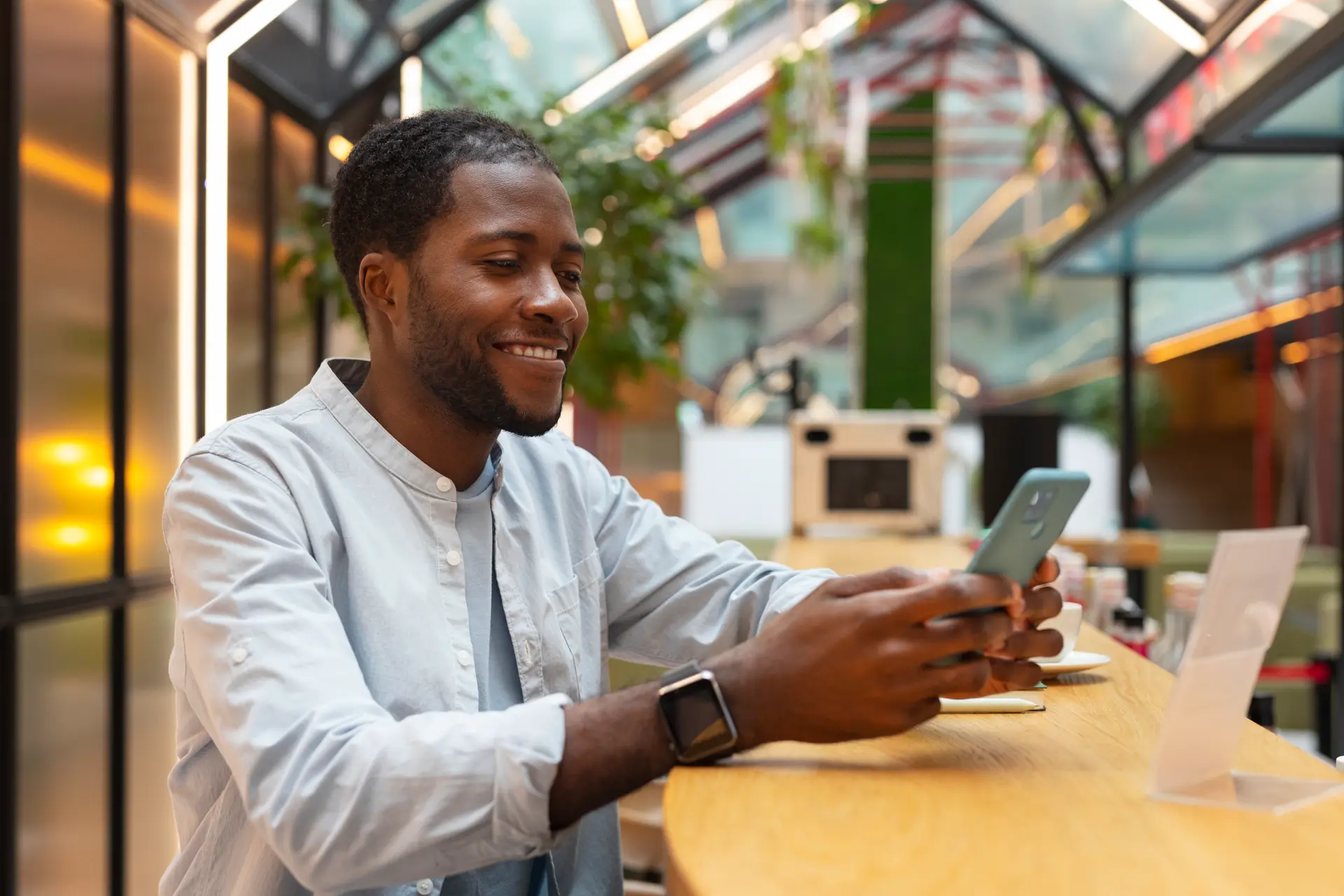 A man smiling at his phone in a bright cafe